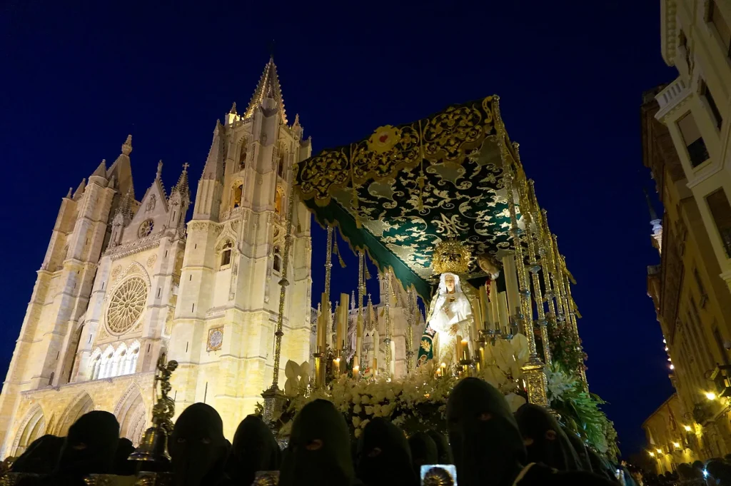Imagen de una procesión nocturna frente a la Catedral de León con trono e integrantes con capillo.