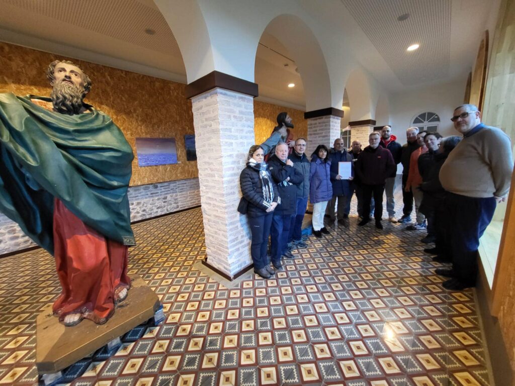 Hermanos de la cofradía junto a una talla religiosa en el interior de un edificio con arcos.