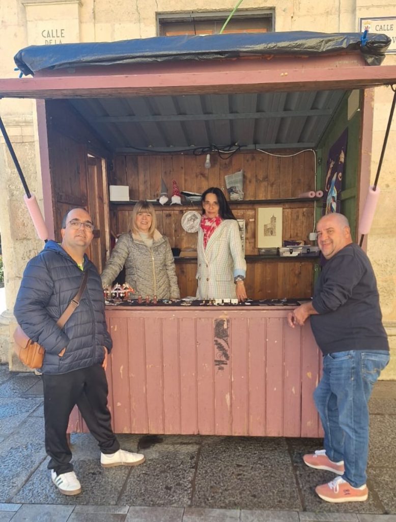 Cuatro personas posan frente a una caseta de madera instalada en la calle junto a una escultura de un león.