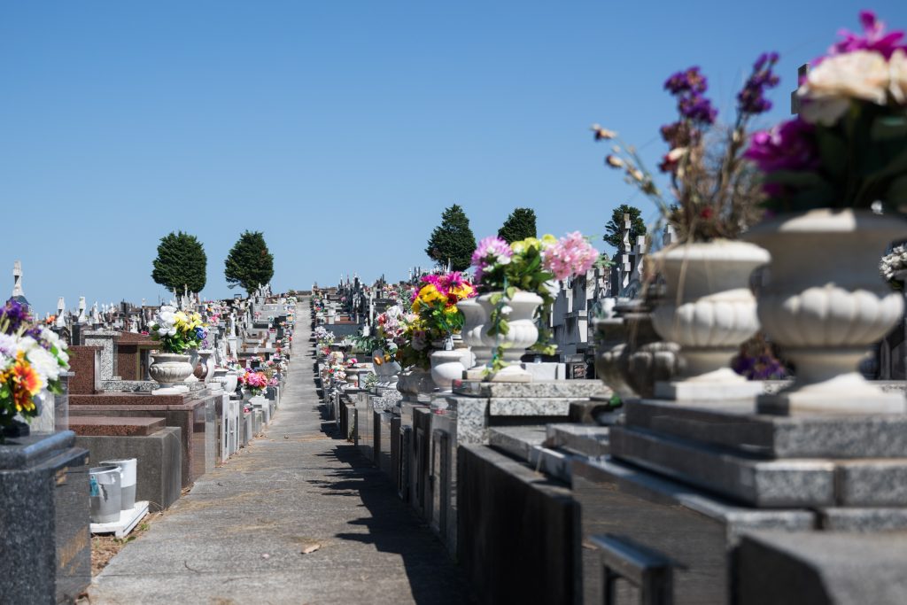 Vista de un cementerio con lápidas y arreglos florales en jarras sobre las sepulturas.